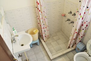 Casa de banho com lavatório, sanita, chuveiro e um pequeno contentor de lixo.