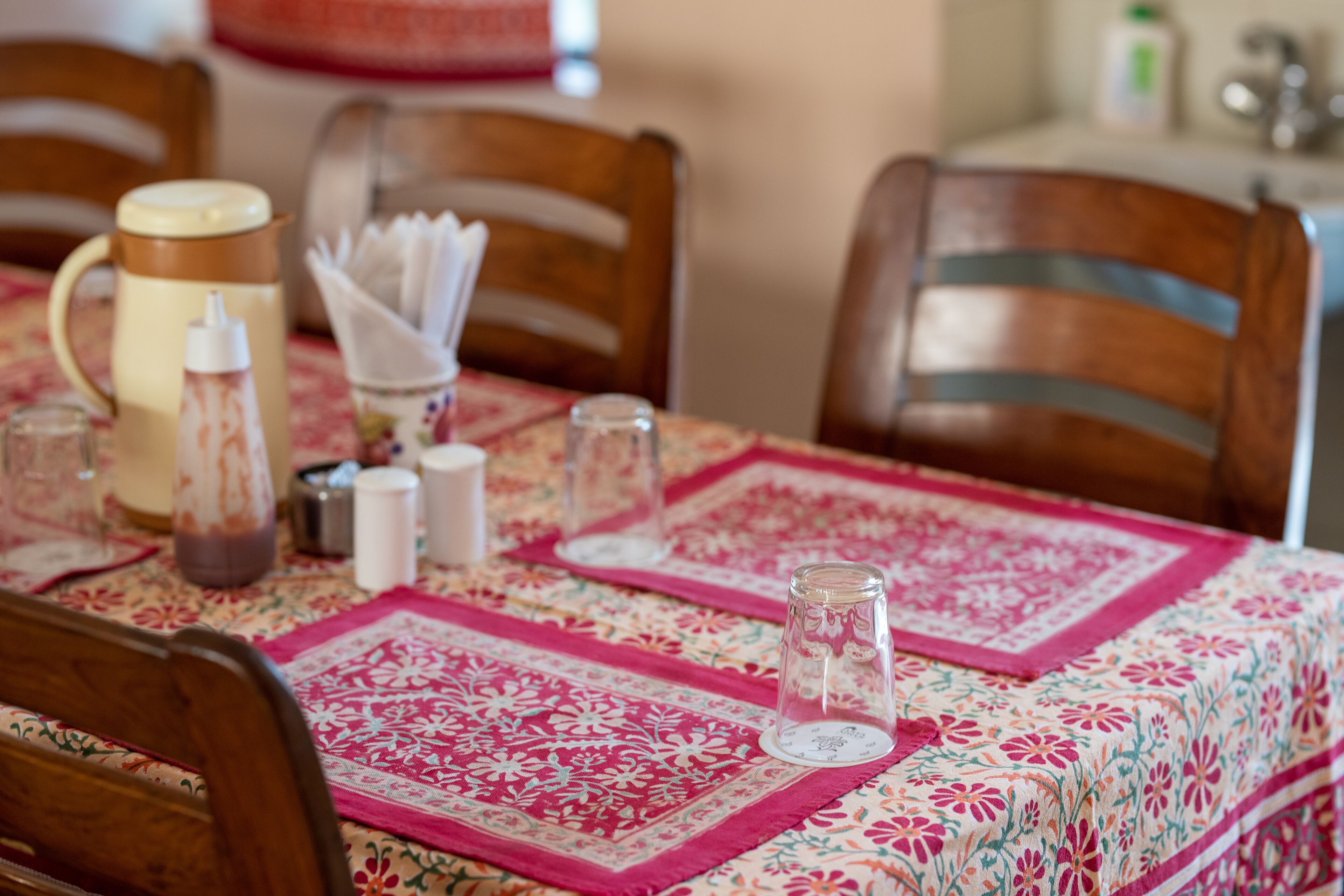 A dining table with a floral tablecloth, a pitcher, and glassware.
