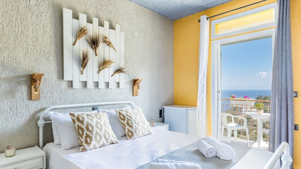 A bedroom with a bed, bedside tables, a wall-mounted decoration, and a balcony with a view. - Hotel Ariadne (Skopelos)