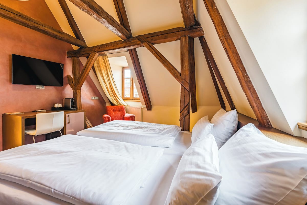 A bedroom with two beds, a desk, a chair, and a TV mounted on the wall.