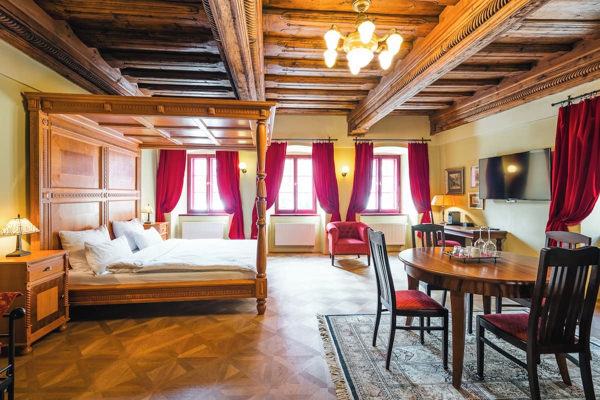 A room with a large bed, a dining table with chairs, and a TV.