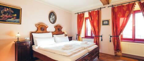 Una cama con dosel de madera con ropa blanca, una mesita de noche con lámpara y un cuadro de frutas en la pared.