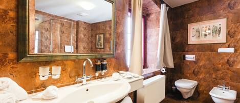 A bathroom with a large mirror, a bathtub, a sink, a bidet, and a framed picture on the wall.