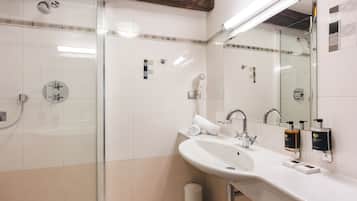 Un baño moderno con ducha envuelta en vidrio, lavamanos blanco con espejo y dos dispensadores de jabón.