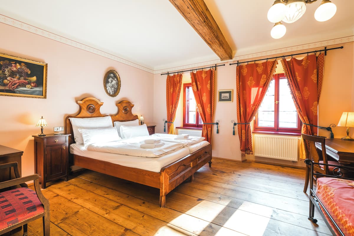 A bedroom with a wooden bed, a desk, a chair, a radiator, and a window with curtains.