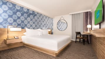 A hotel room with a large bed, a desk, a chair, a TV, a lamp, and a patterned wall.