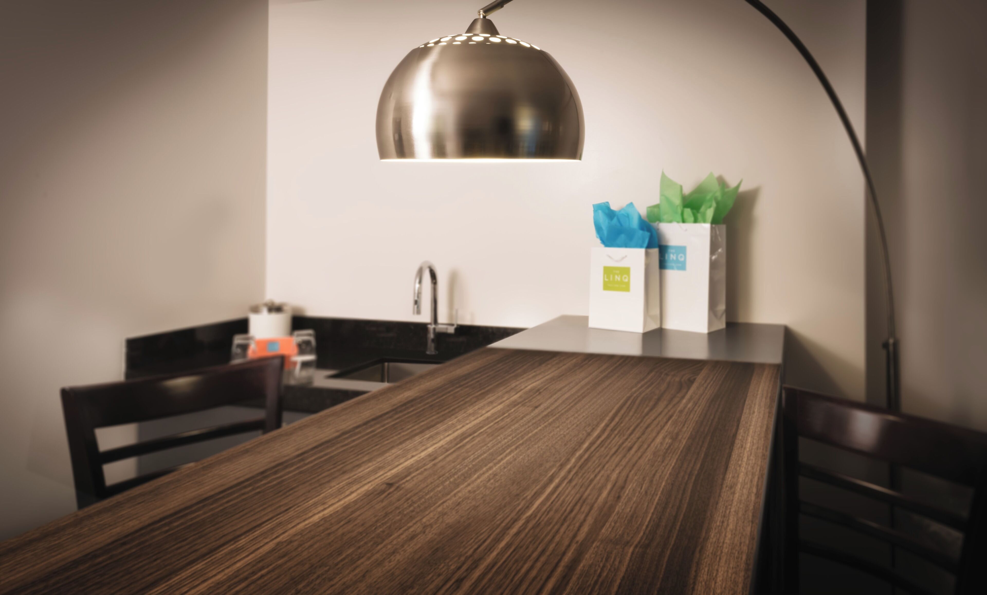 A modern kitchen with a wooden dining table, a stainless steel sink, and a pendant light.