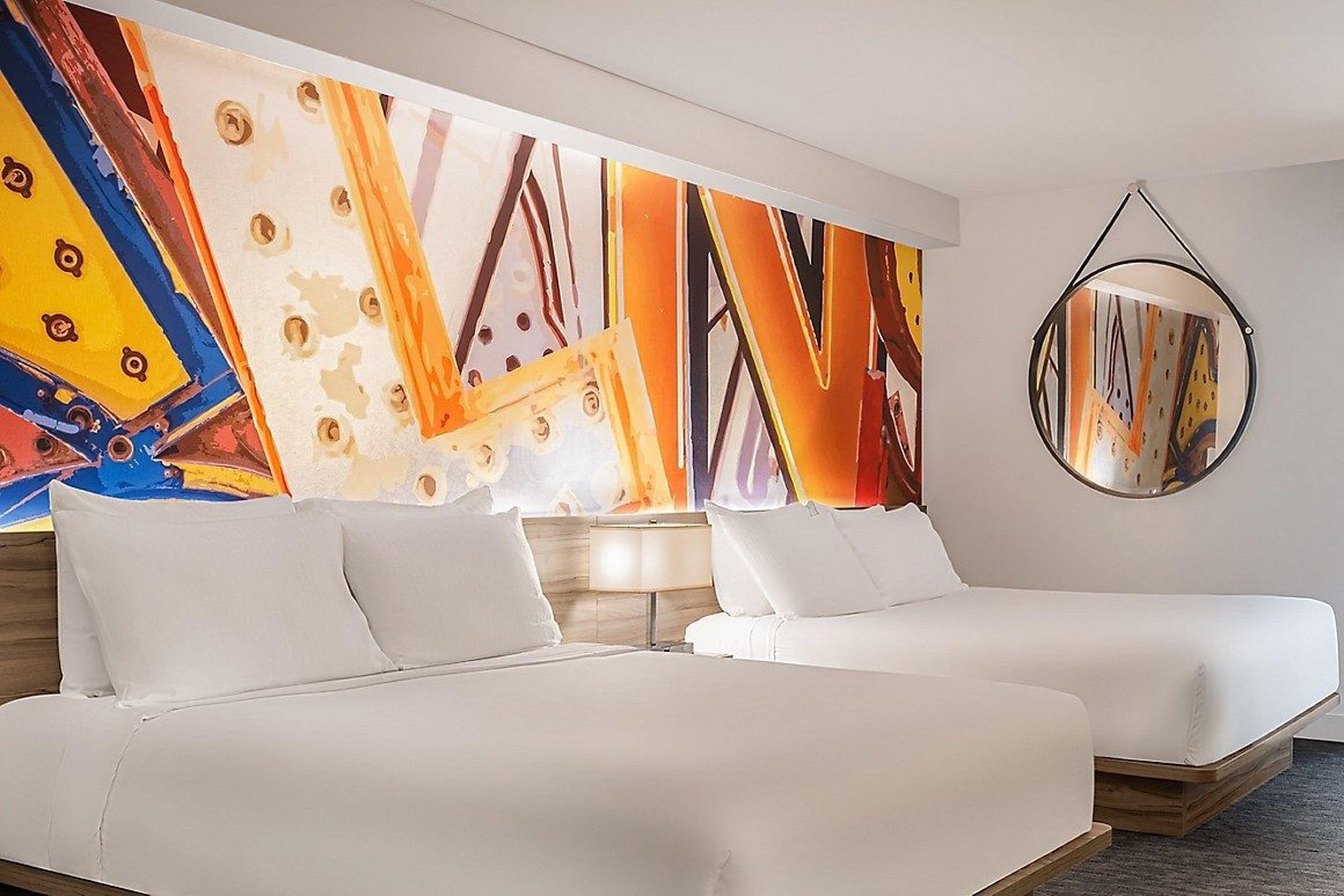 Habitación de hotel con dos camas, un cuadro abstracto grande en la pared y un espejo redondo.
