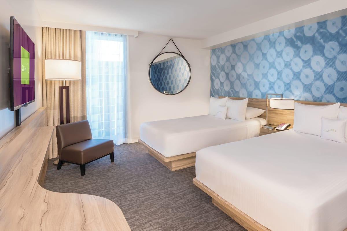 A hotel room with two beds, a desk, a chair, a TV, and a bathroom.
