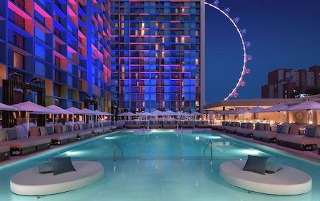 A hotel with a large pool, lounge areas with umbrellas, and a Ferris wheel in the background.