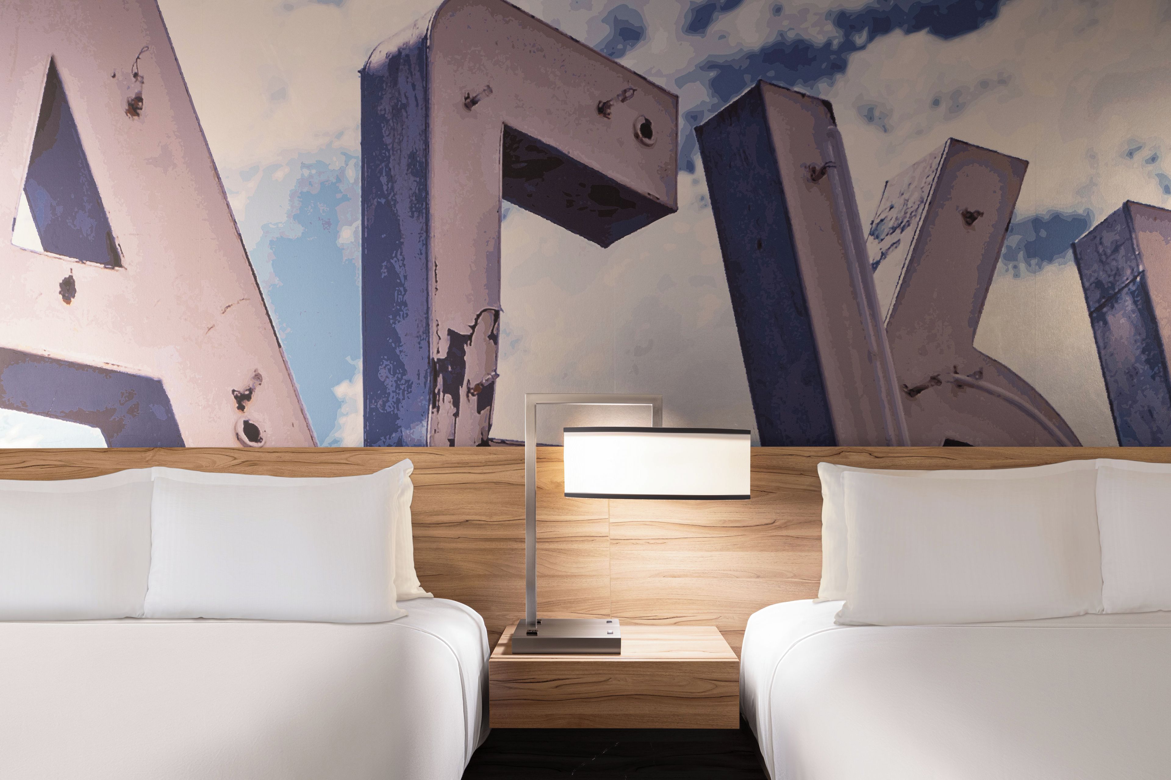 A hotel room with two beds, a nightstand with a lamp, and a wall mural.