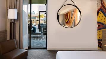 A hotel room with a bed, a sofa, a lamp, a mirror, and a view of the outdoor seating area.