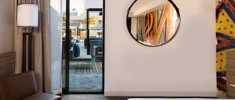 A hotel room with a bed, a sofa, a lamp, a mirror, and a view of the outdoor seating area.