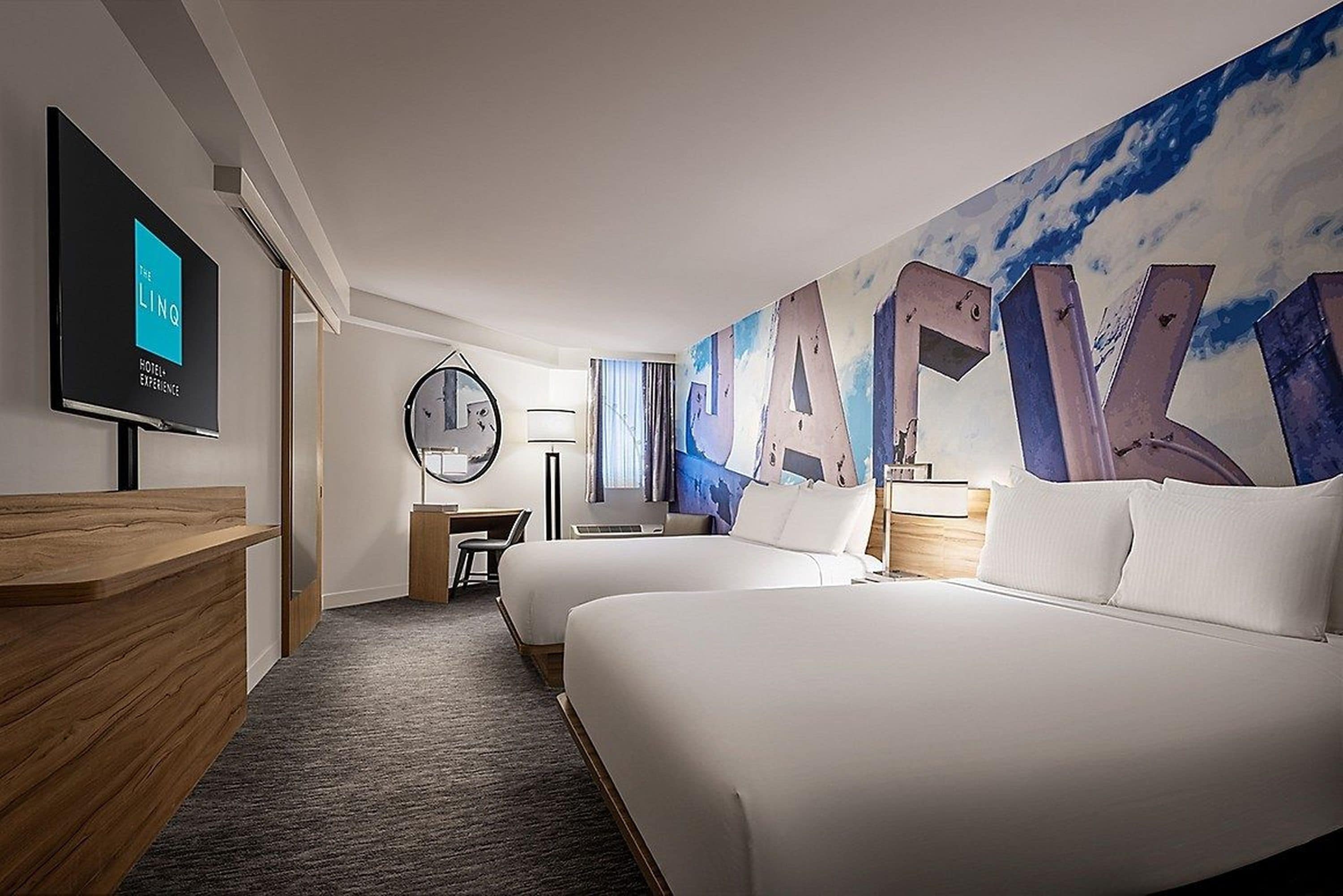 Une chambre d’hôtel avec deux lits, un bureau, une télévision et un grand tableau abstrait accroché au mur.