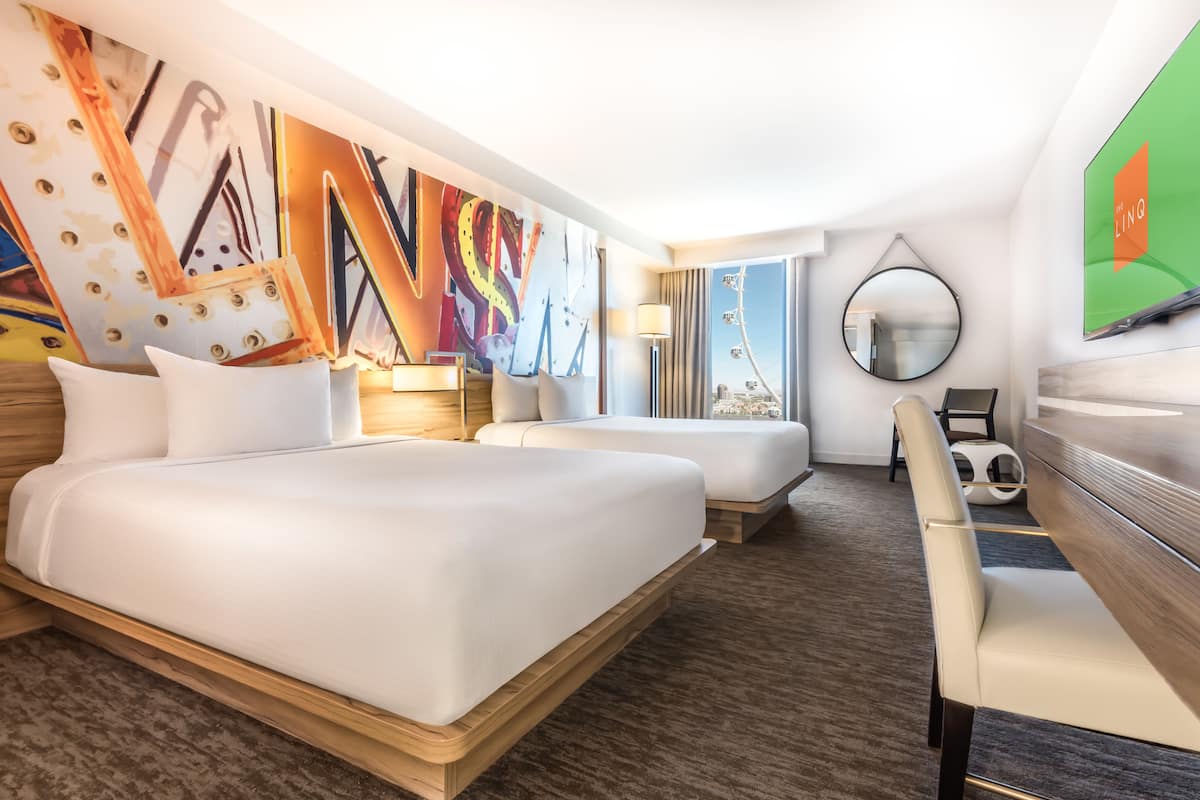 A hotel room with two beds, a desk, a chair, a TV, a large abstract painting, and a view of a cityscape.