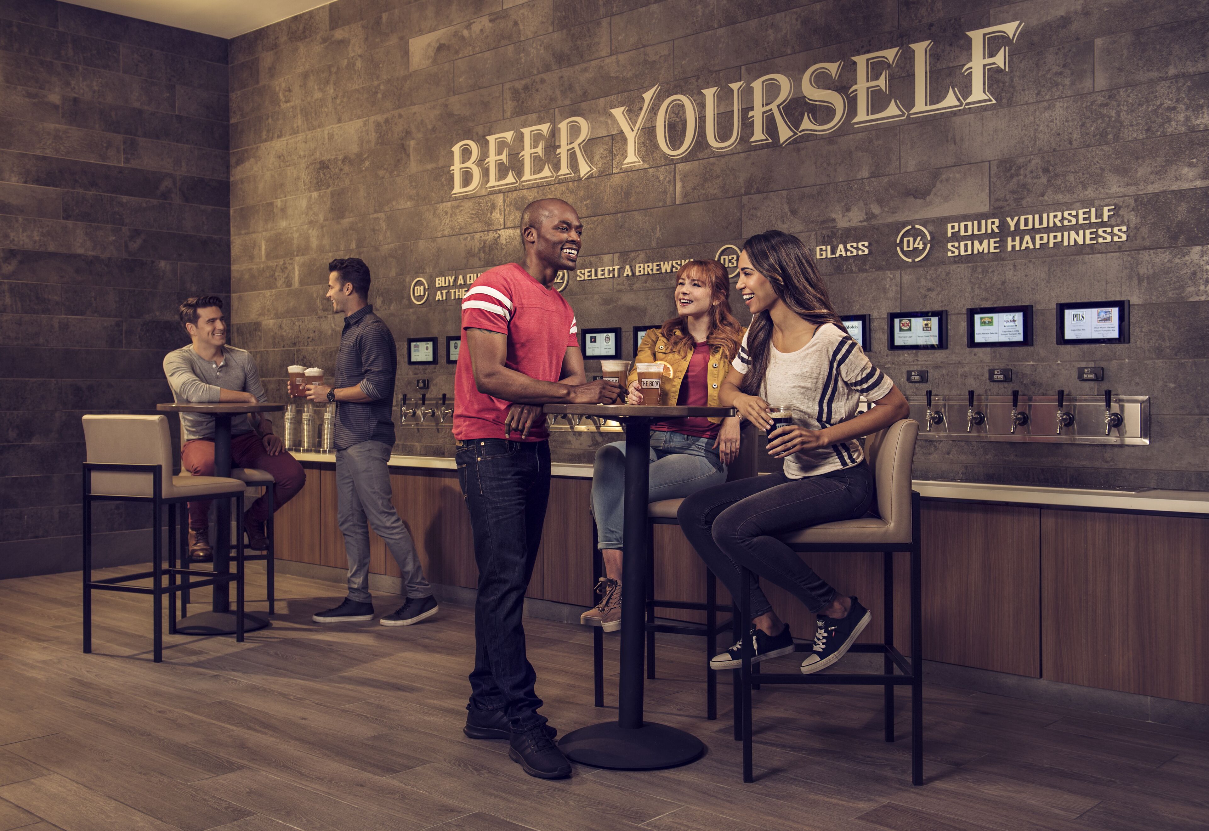 A bar area with a 'Beer Yourself' sign, bar stools, and a counter with taps.