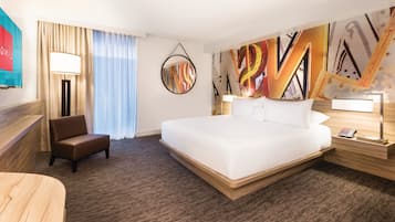 Una habitación de hotel con una cama grande, un escritorio, una silla y una pared con arte abstracto.