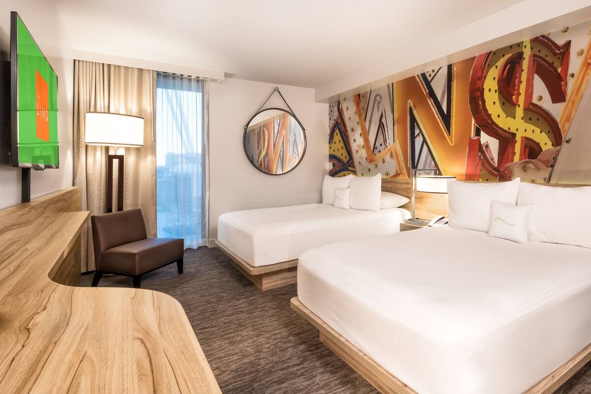 A hotel room with two beds, a desk, a chair, a TV, and a large abstract painting on the wall.