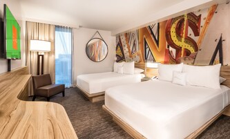 A hotel room with two beds, a desk, a chair, a TV, and a large abstract painting on the wall.