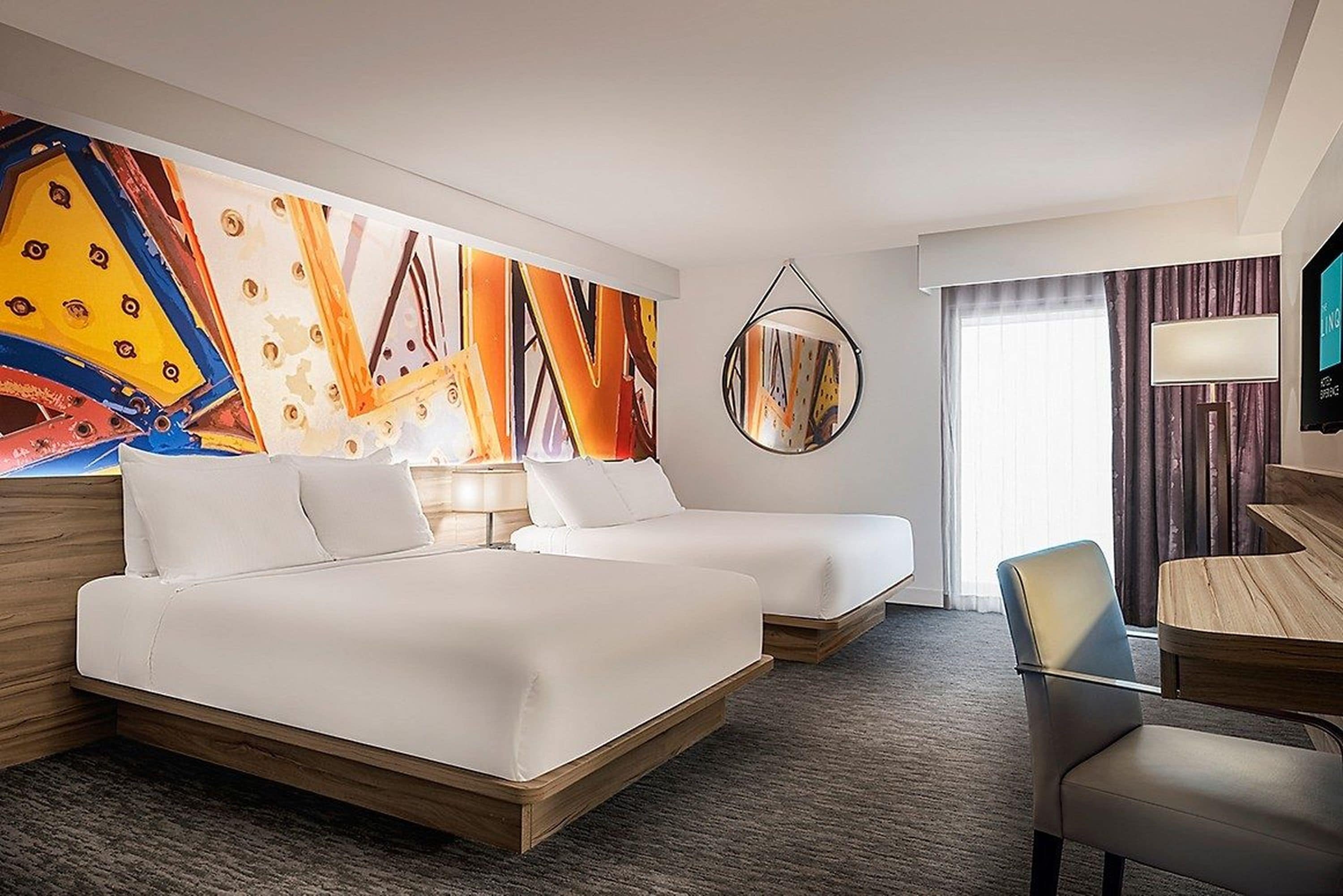 Habitació d'hotel amb dos llits, un escriptori, una cadira, un televisor i un quadre abstracte gran a la paret.