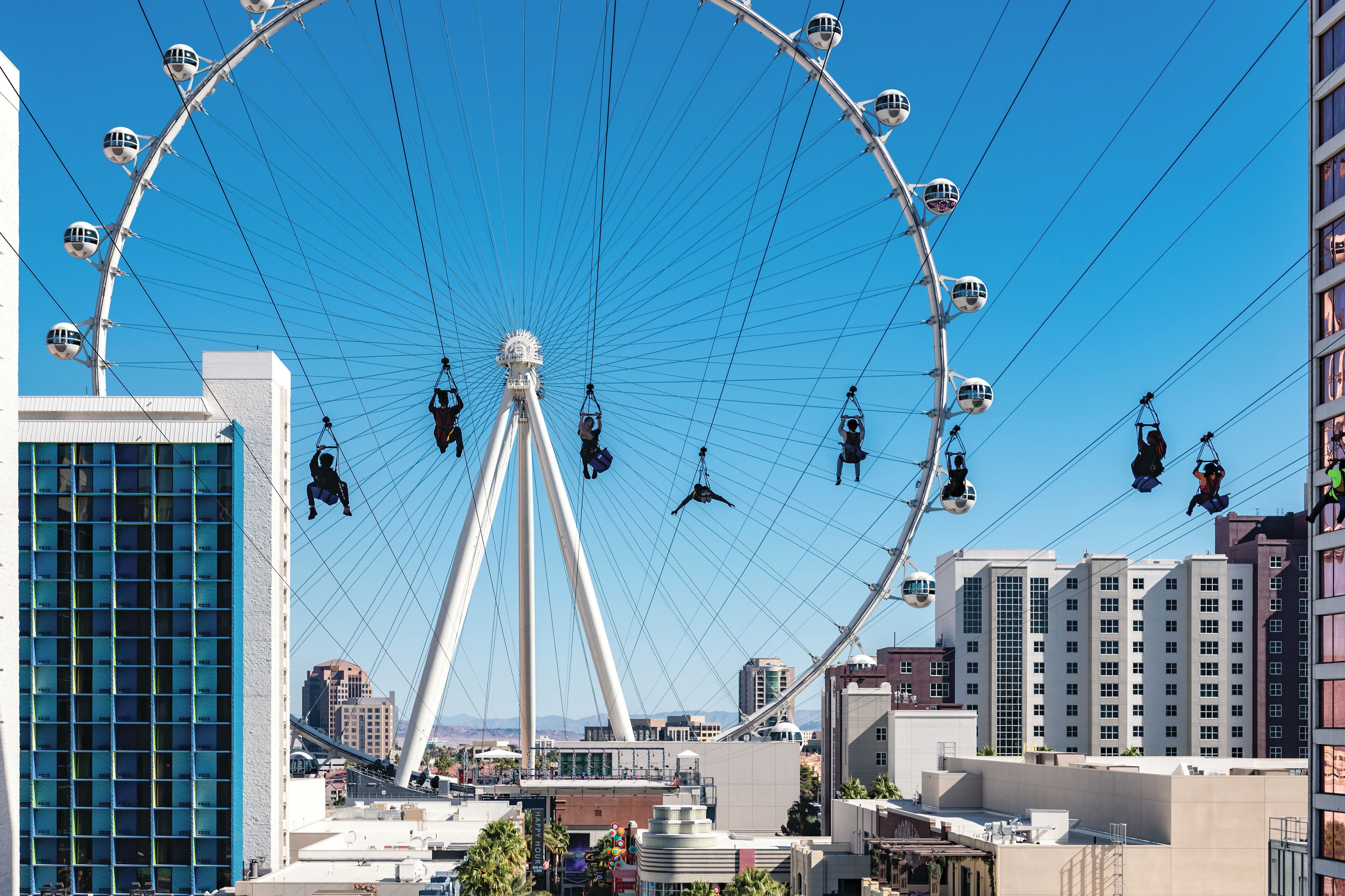 A large Ferris wheel with gondolas, surrounded by modern buildings and a clear blue sky.