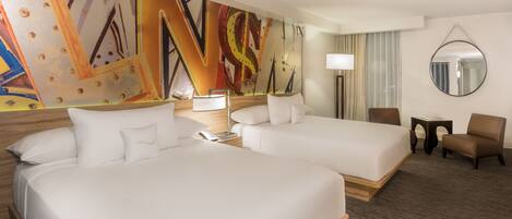 A hotel room with two beds, a large abstract painting on the wall, a round mirror, and a small table with a lamp.