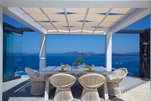 A table set for two with wicker chairs, a glass top, and a view of the sea. - Cavo Ventus Villa - Adults Only (Santorini)