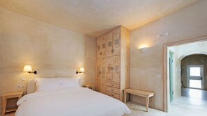 A bedroom with a large bed, wooden wardrobe, two bedside tables, and a bench. - Cavo Ventus Villa - Adults Only (Santorini)