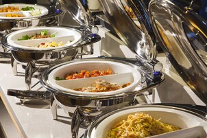A buffet with multiple dishes, including pasta and salads, served in stainless steel chafing dishes.