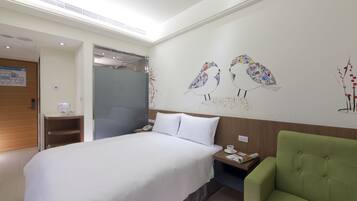 A hotel room with a large bed, a green armchair, a nightstand with a phone and a cup, and a wall with bird artwork.