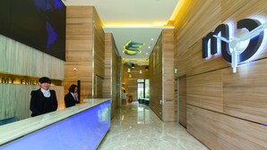 Un área de recepción de hotel moderna con interior de madera, una mesa de recepción y un logotipo visible en la pared.