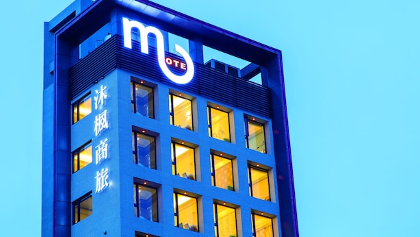 Un edificio moderno con un llamativo letrero que dice 'MOTEL', múltiples ventanas y fachada azul.