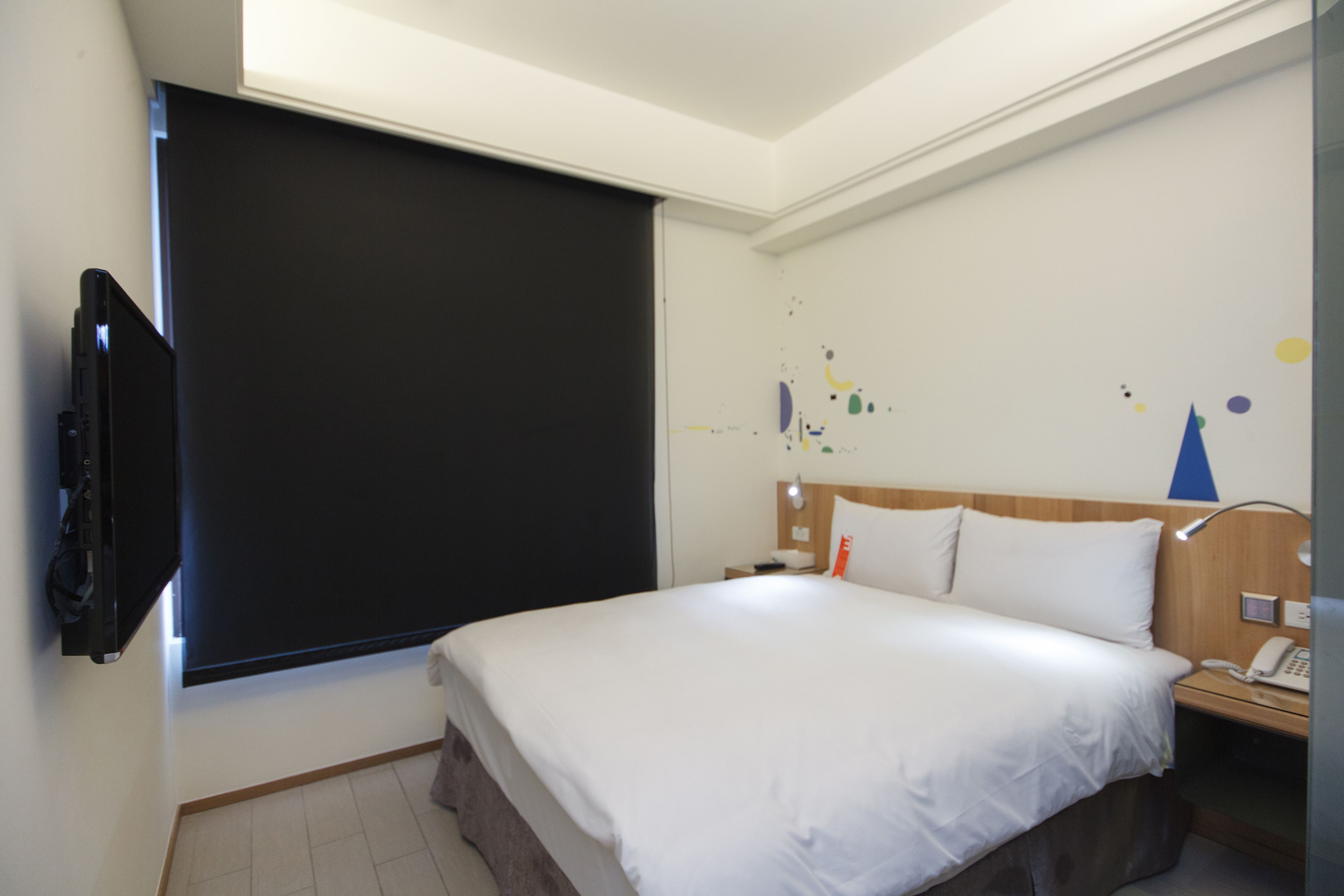 Habitación de hotel con una cama grande, un televisor de pantalla plana montado en la pared, una mesita de noche con lámpara y una pared decorada con arte abstracto.