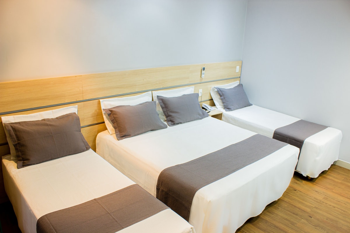 A hotel room with three single beds, each with a pillow and a blanket.