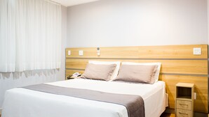A neatly made bed with a wooden headboard, a bedside table with a lamp, and a small drawer unit. - Imperial Plaza Hotel (Samambaia)