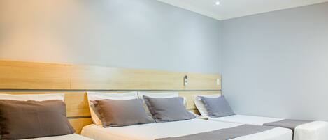 A hotel room with three beds, each with a white and brown bedspread, and a wooden headboard.