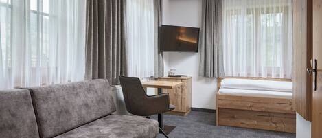 A modern hotel room with a sofa, a wooden desk, a bed, and a TV mounted on the wall.