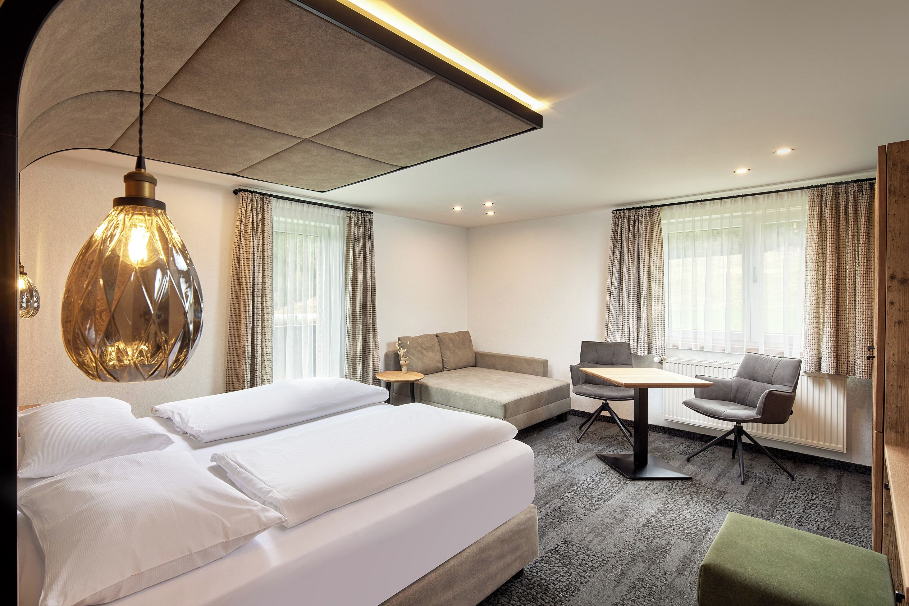 A hotel room with a bed, a sofa, a dining table, and a chair.