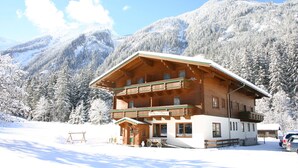 A wooden chalet with a balcony, surrounded by snow-covered mountains. - Hotel Gasthof Siggen (Neukirchen am Grossvenediger)
