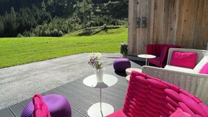 A wooden deck with a wicker chair and ottoman, a small table with a vase, and a view of a mountain. - Hotel Gasthof Siggen (Neukirchen am Grossvenediger)