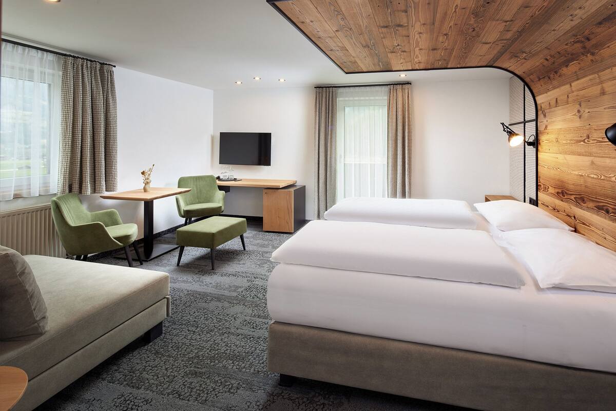 A hotel room with a bed, a desk, two chairs, a television, and a window with curtains.