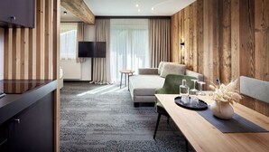 A modern hotel room with a wooden accent wall, a sofa, a dining table with a vase, and a TV mounted on the wall. - Hotel Gasthof Siggen (Neukirchen am Grossvenediger)