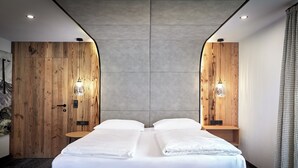 A modern hotel room with a large bed, wooden walls, and two bedside tables with lamps. - Hotel Gasthof Siggen (Neukirchen am Grossvenediger)