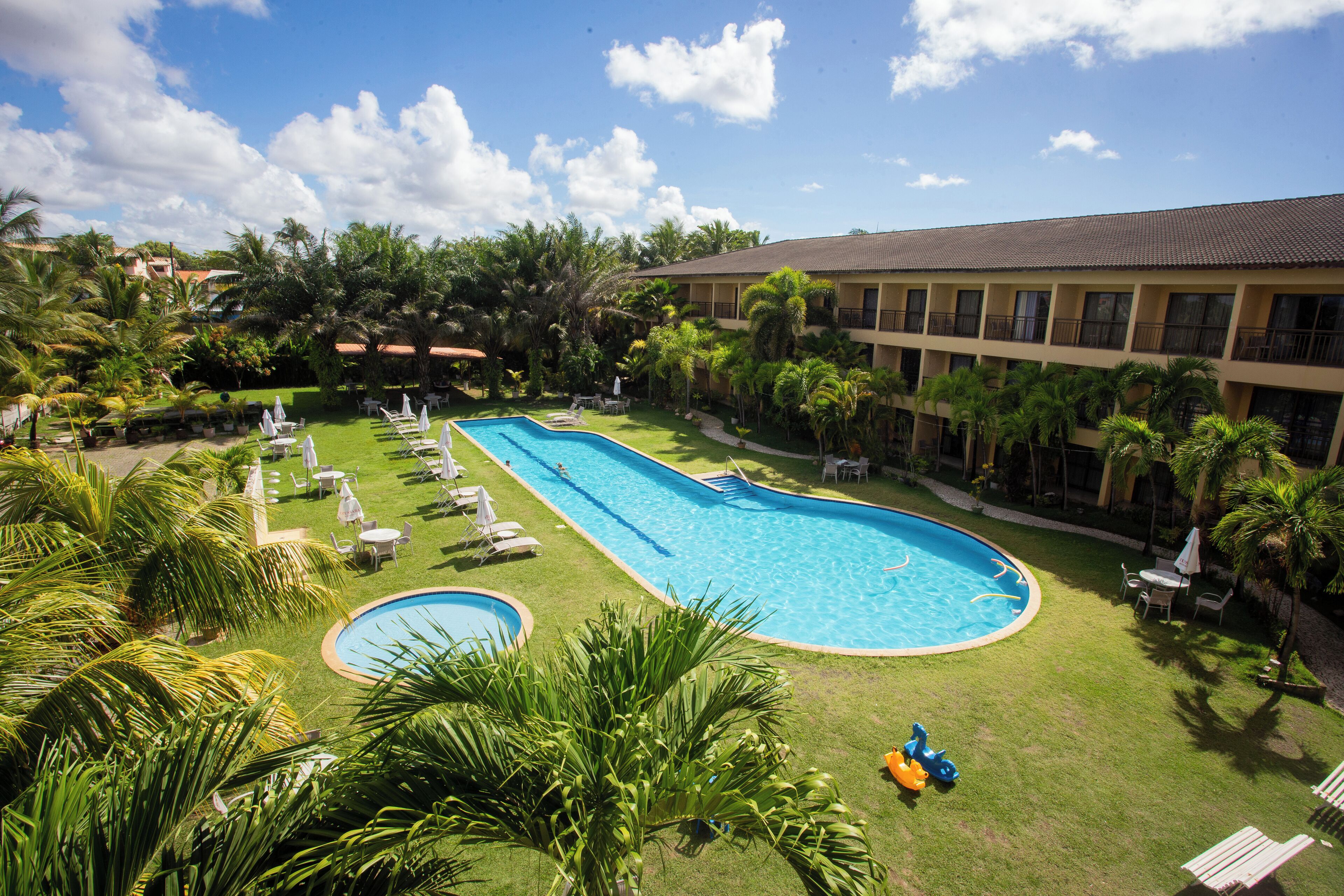 Une grande piscine entourée de palmiers et de chaises longues, avec un bâtiment en arrière-plan.