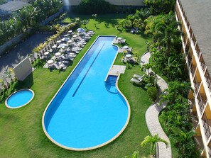 A swimming pool with a long, narrow shape surrounded by a well-maintained lawn, several lounge chairs, and umbrellas. - Catussaba Business (Salvador)