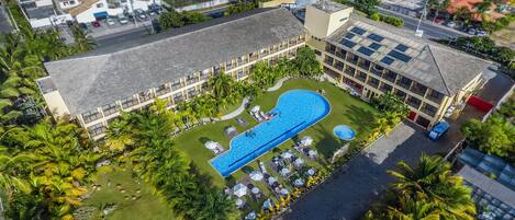A hotel with a swimming pool, multiple balconies, and lush greenery.