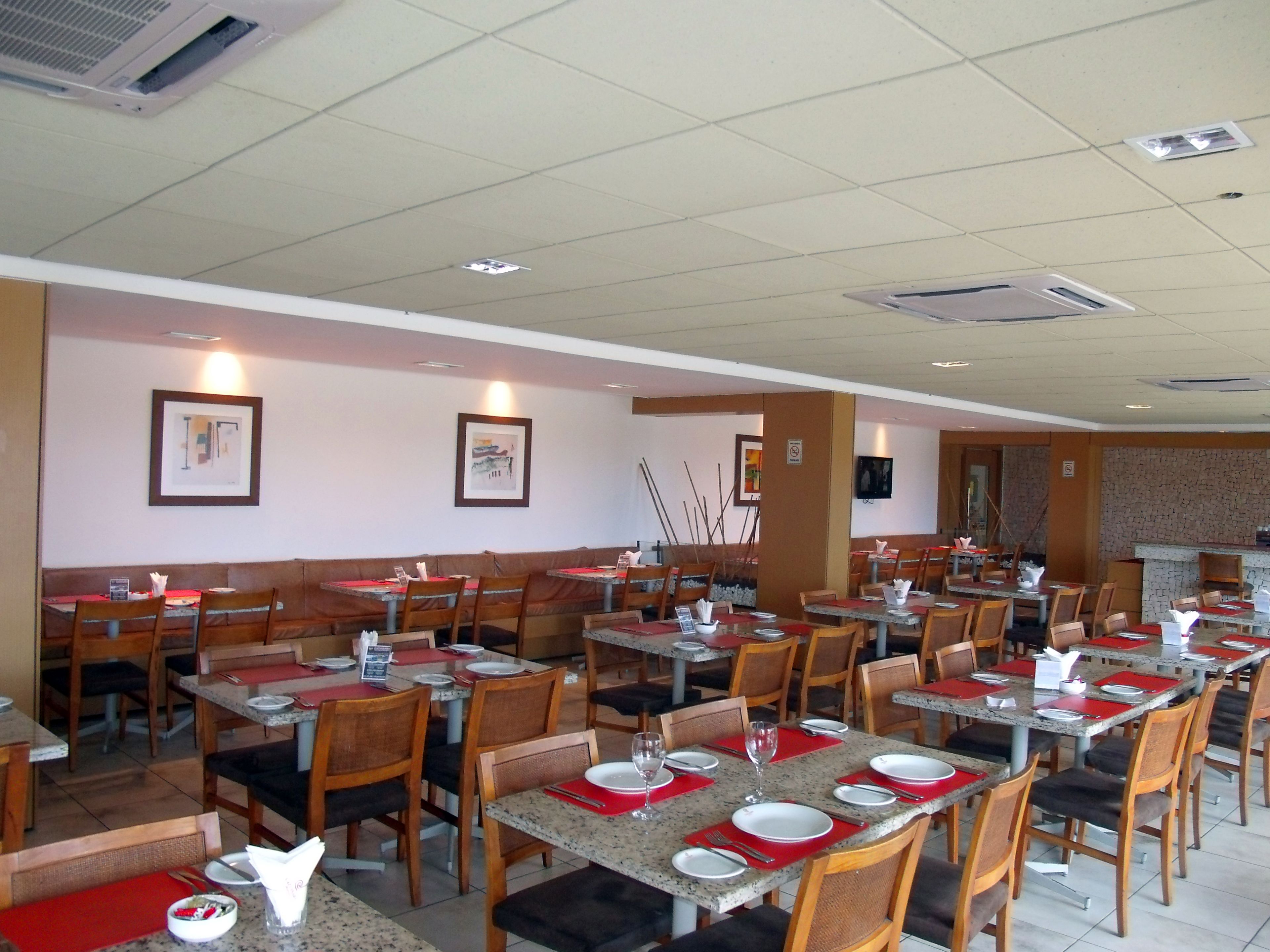 A restaurant with multiple tables and booths, equipped with red placemats and white plates.