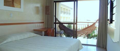 Une chambre d’hôtel avec un grand lit, un bureau, une chaise, une télévision et un balcon équipé d’un hamac.