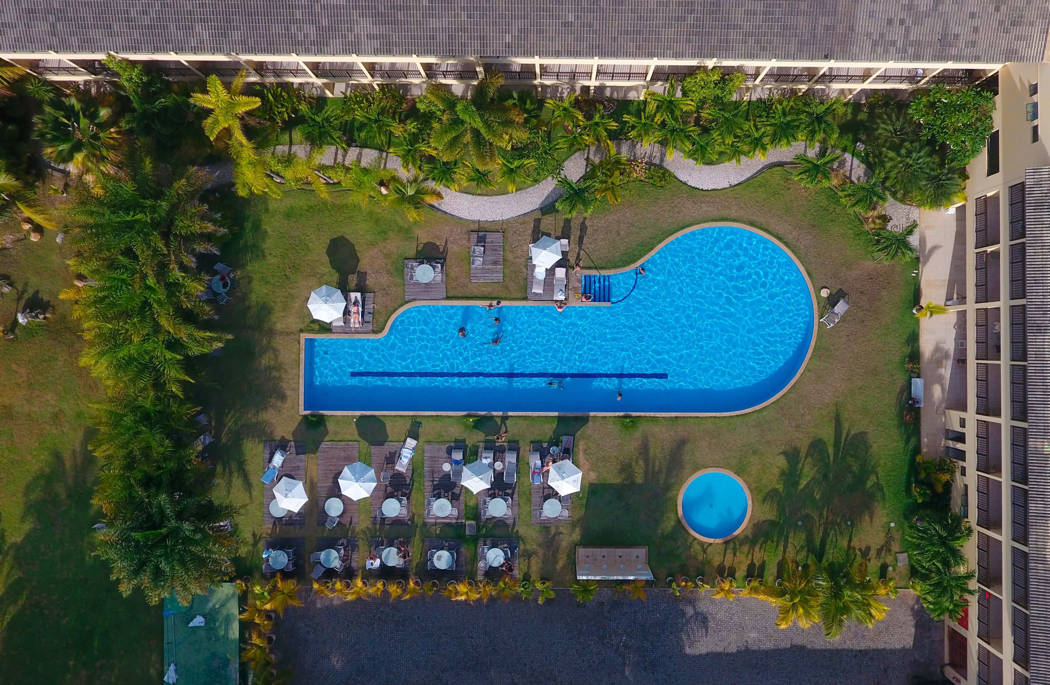 An aerial view of a resort with a large swimming pool, sun loungers, and a small circular pool.