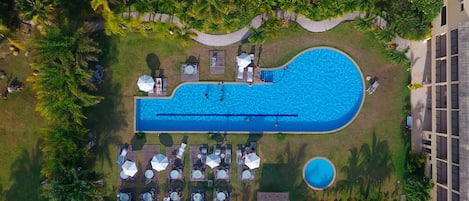 Vista aérea de un complejo turístico con una piscina grande, tumbonas y una piscina circular pequeña.